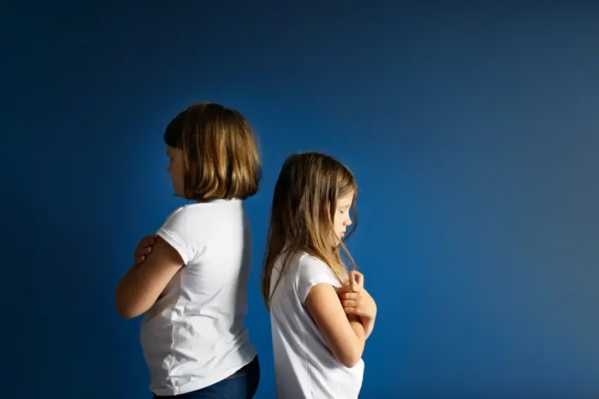 two children standing back to back looking upset and distant